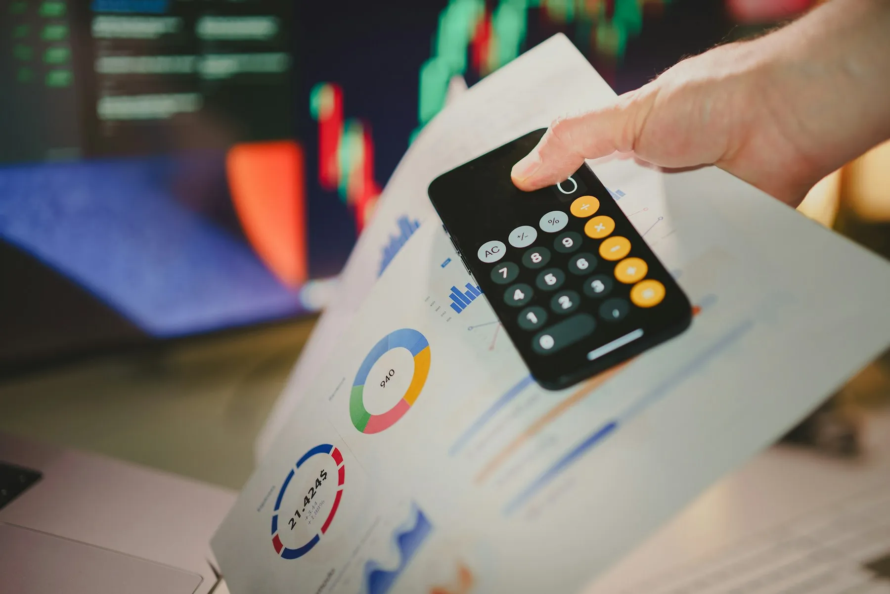 Hand using a calculator over financial reports with charts