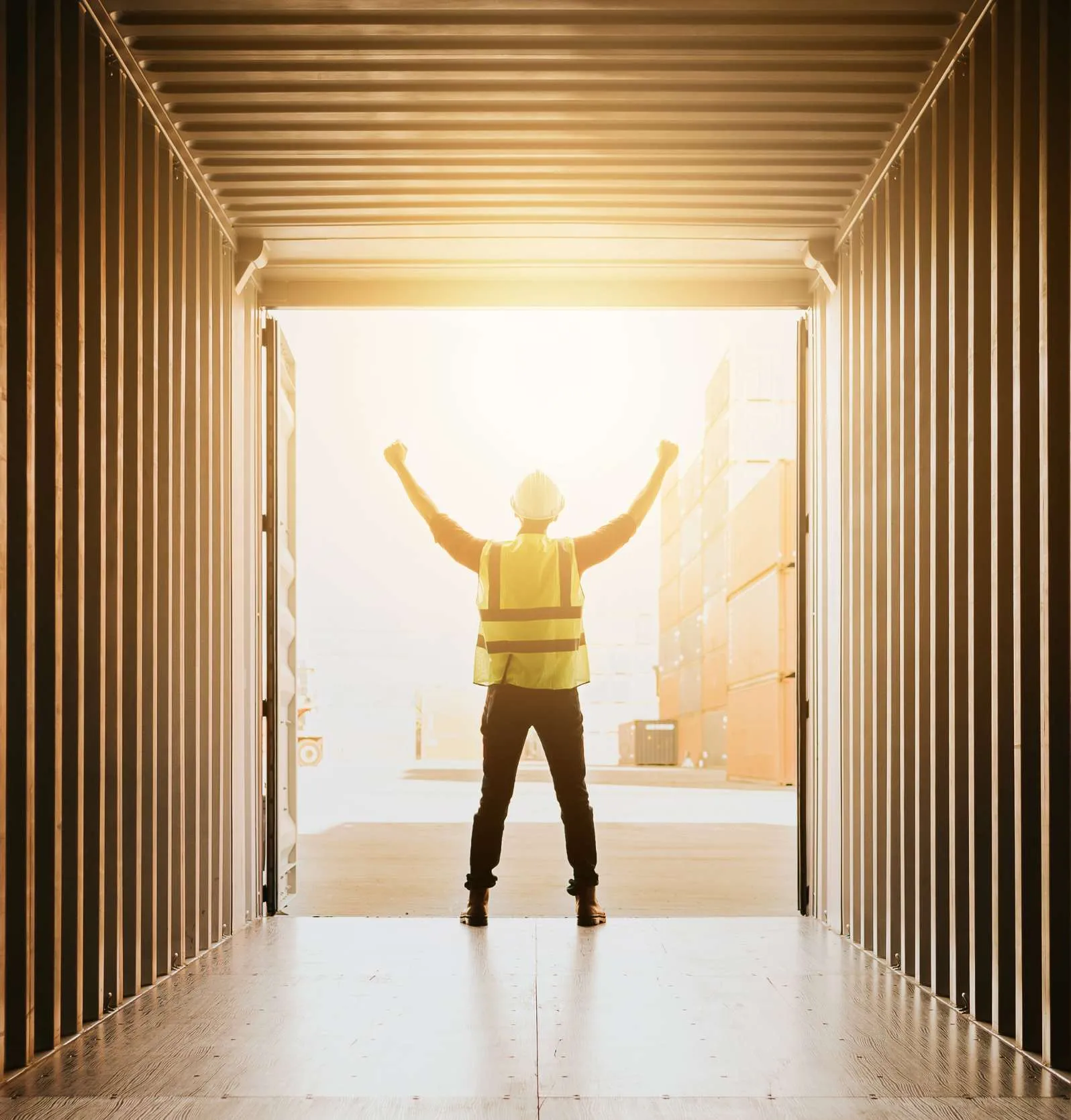 Worker raising his arms in celebration at the open doors of a shipping container